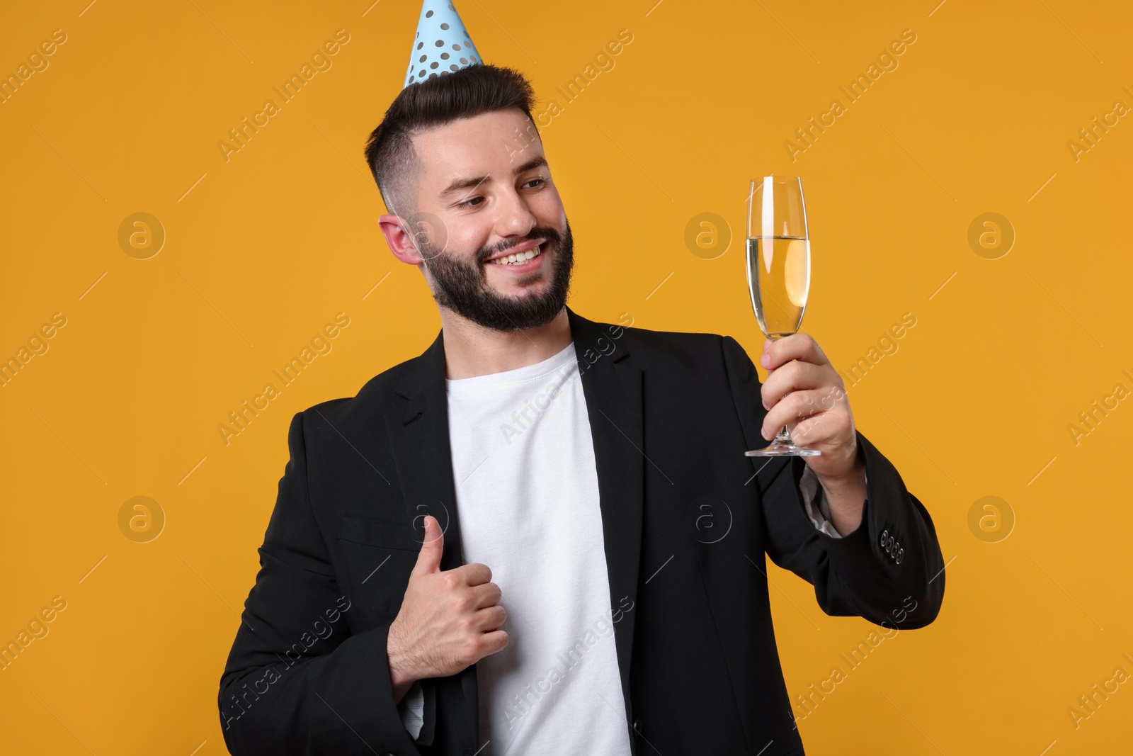 Happy Birthday. Handsome man with party hat and champagne showing thumbs up on orange background Photo of Happy Birthday. Handsome man with party hat and champagne showing thumbs up on orange background