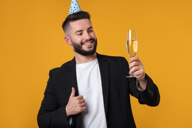 Photo of Happy Birthday. Handsome man with party hat and champagne showing thumbs up on orange background