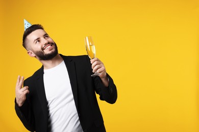 Photo of Happy Birthday. Handsome man with party hat and champagne on orange background, space for text