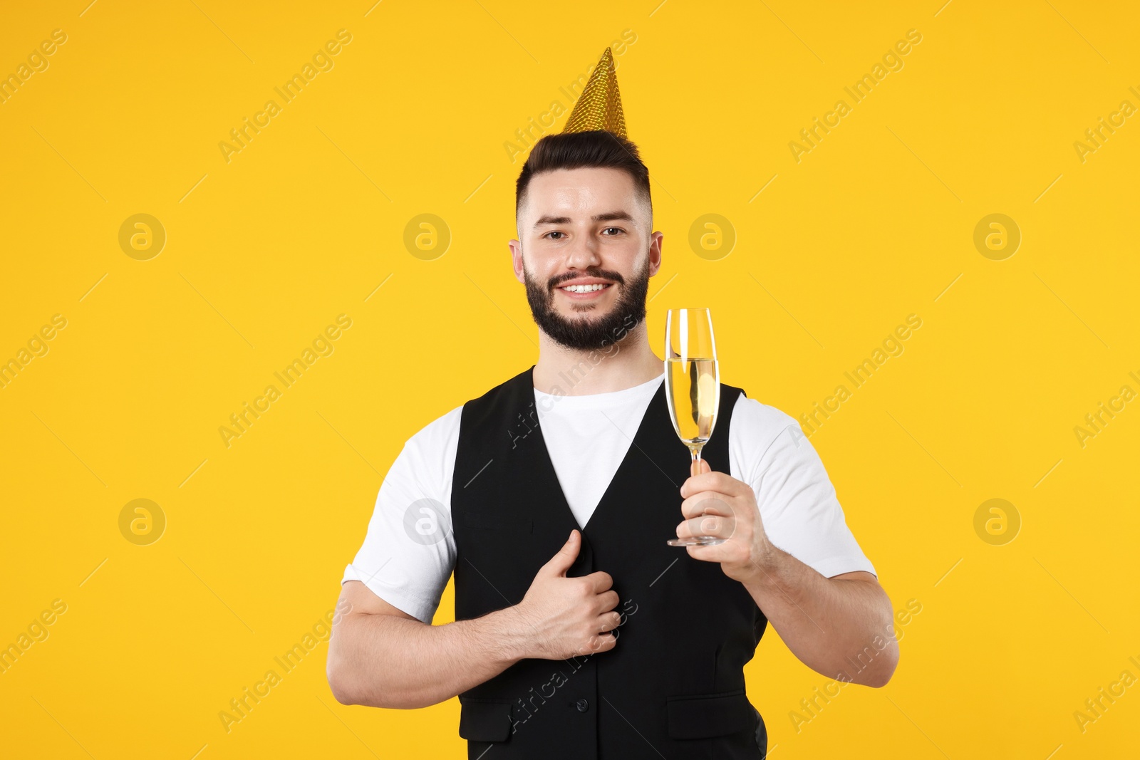Happy Birthday. Handsome man with party hat and glass of champagne showing thumbs up on orange background Photo of Happy Birthday. Handsome man with party hat and glass of champagne showing thumbs up on orange background