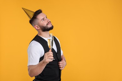 Photo of Happy Birthday. Handsome man with party hat and glass of champagne on orange background, space for text