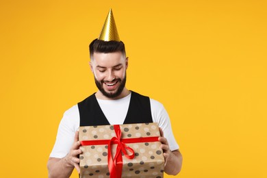 Photo of Happy Birthday. Handsome man with party hat and gift box on orange background, space for text