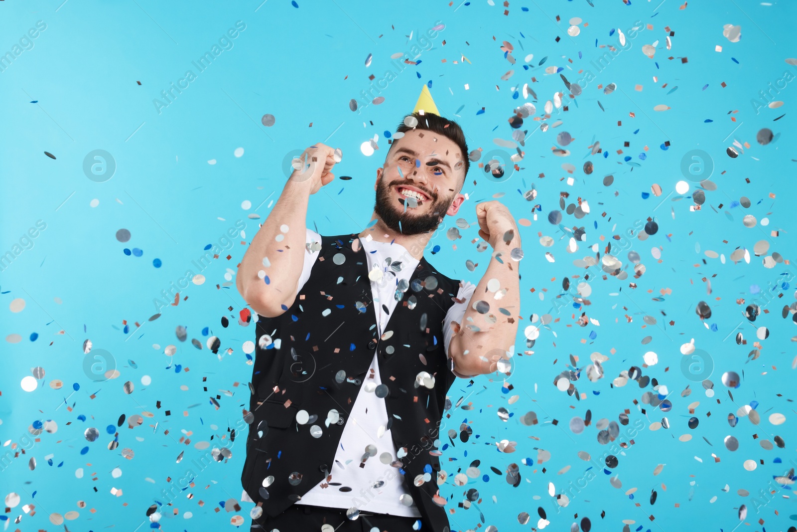 Happy Birthday. Handsome man with party hat under confetti shower on light blue background Photo of Happy Birthday. Handsome man with party hat under confetti shower on light blue background