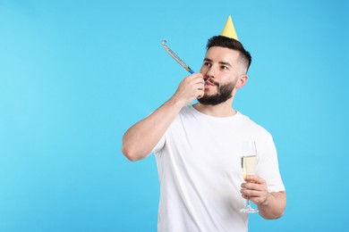 Photo of Happy Birthday. Handsome man with party hat, blower and glass of champagne on light blue background, space for text