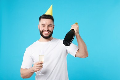 Photo of Happy Birthday. Handsome man with party hat and champagne on light blue background, space for text