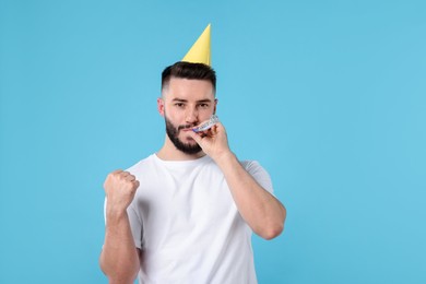 Photo of Happy Birthday. Handsome man with party hat and blower on light blue background, space for text