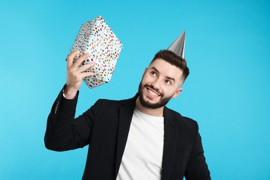 Photo of Happy Birthday. Handsome man with party hat and gift box on light blue background