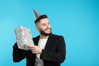 Photo of Happy Birthday. Handsome man with party hat and gift box on light blue background, space for text