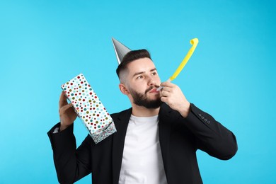 Photo of Happy Birthday. Handsome man with party hat, blower and gift box on light blue background