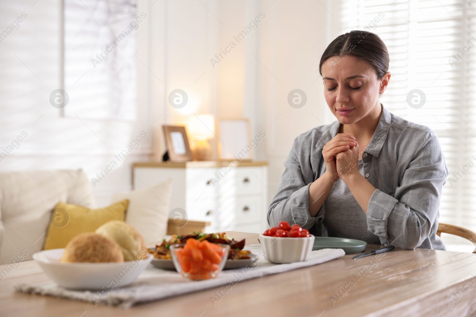 Woman praying before dinner at table indoors. Space for text Photo of Woman praying before dinner at table indoors. Space for text
