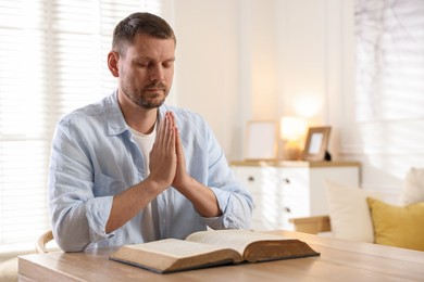 Photo of Man with Bible praying at table indoors. Space for text
