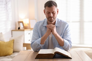 Photo of Man with Bible praying at table indoors