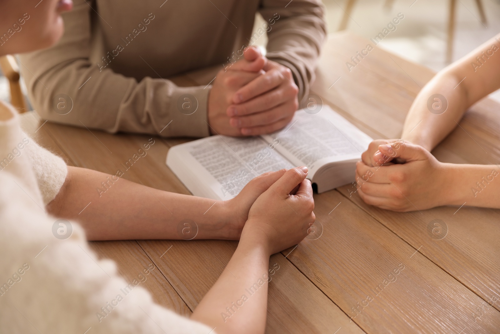 Family with Bible praying at table indoors, closeup Photo of Family with Bible praying at table indoors, closeup