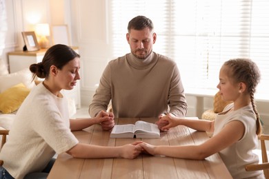 Photo of Family with Bible praying at table indoors