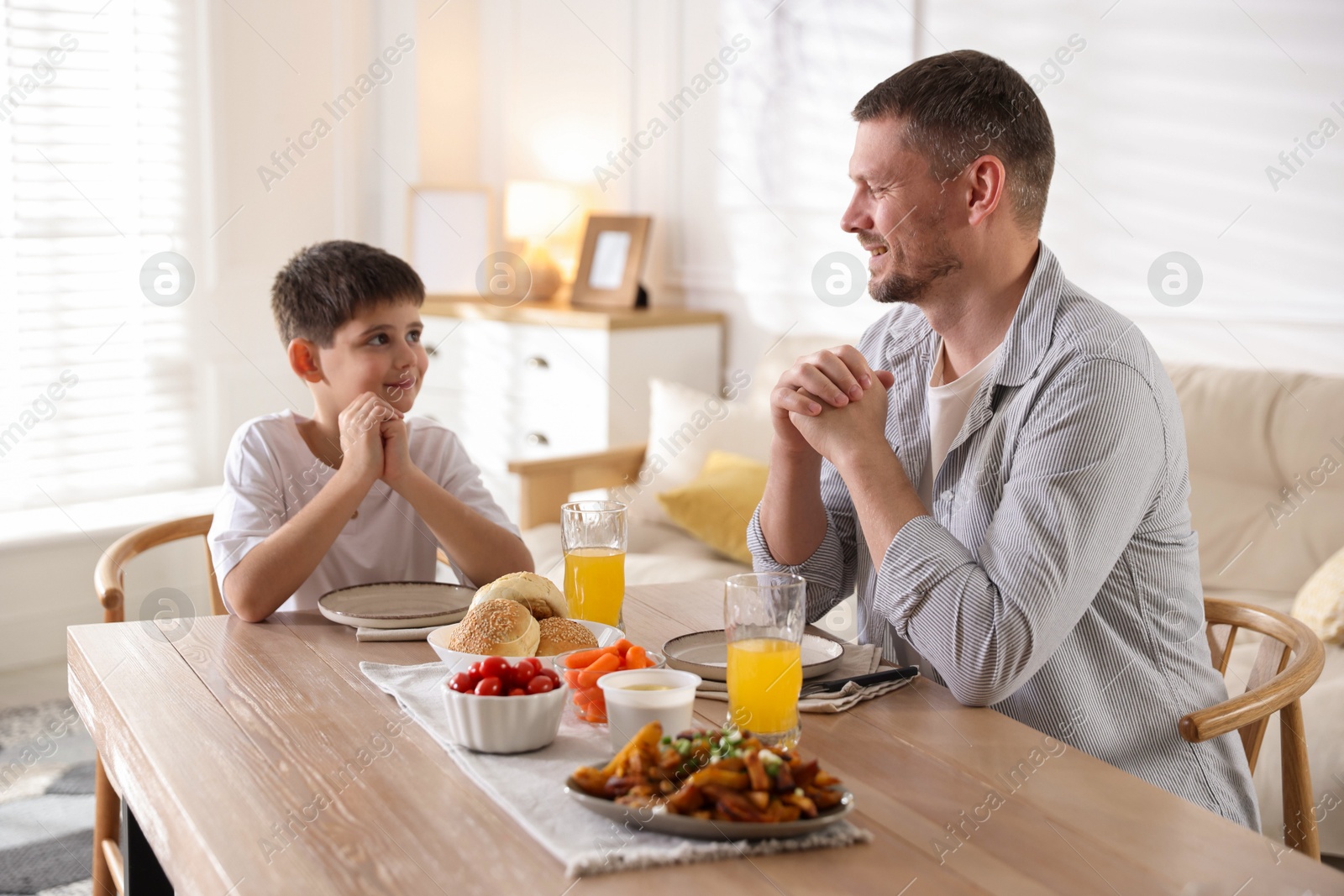 Father and son praying before dinner at table indoors Photo of Father and son praying before dinner at table indoors