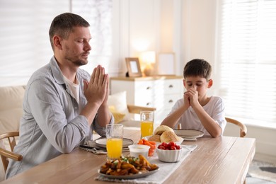 Photo of Father and son praying before dinner at table indoors