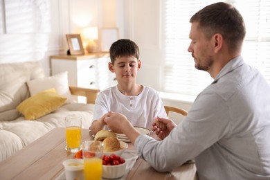 Photo of Father and son praying before dinner at table indoors