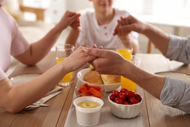Photo of Family praying together before dinner at table indoors, closeup