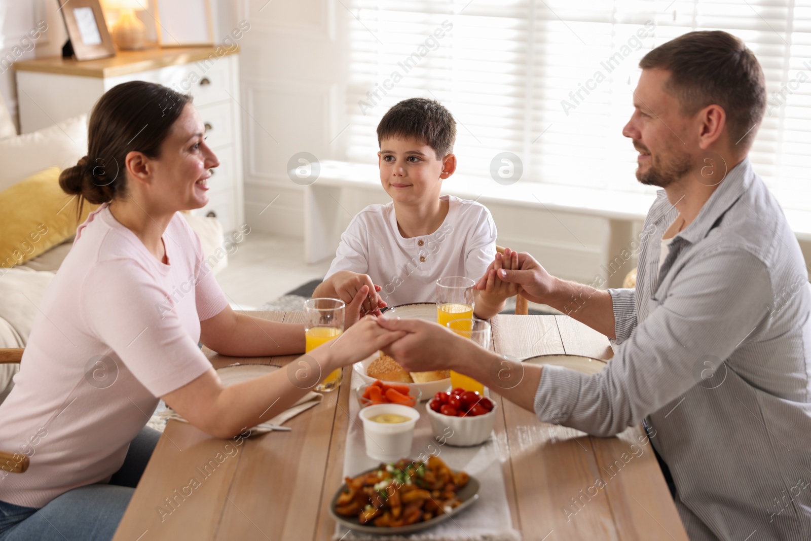 Family praying together before dinner at table indoors Photo of Family praying together before dinner at table indoors