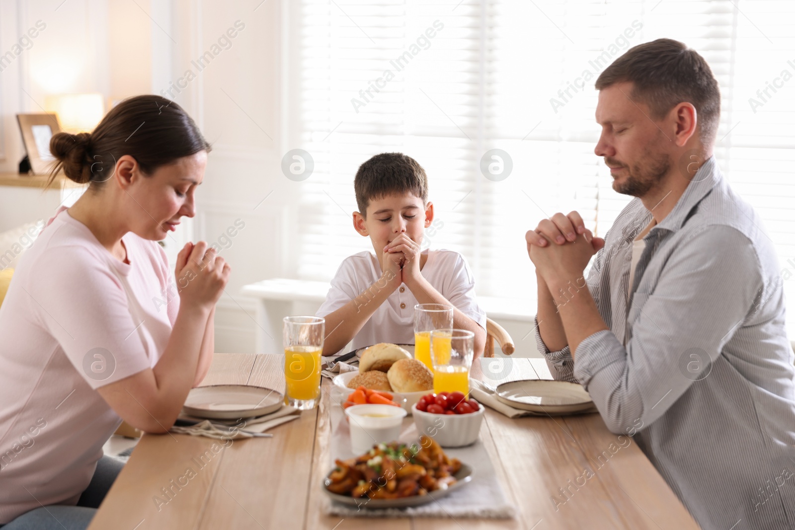Family praying together before dinner at table indoors Photo of Family praying together before dinner at table indoors