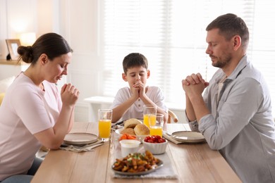 Photo of Family praying together before dinner at table indoors