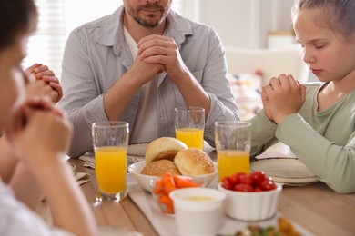 Photo of Family praying together before dinner at table indoors, closeup