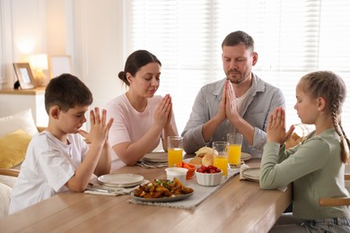 Photo of Family praying together before dinner at table indoors