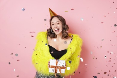Photo of Birthday celebration. Woman with gift and confetti on pink background