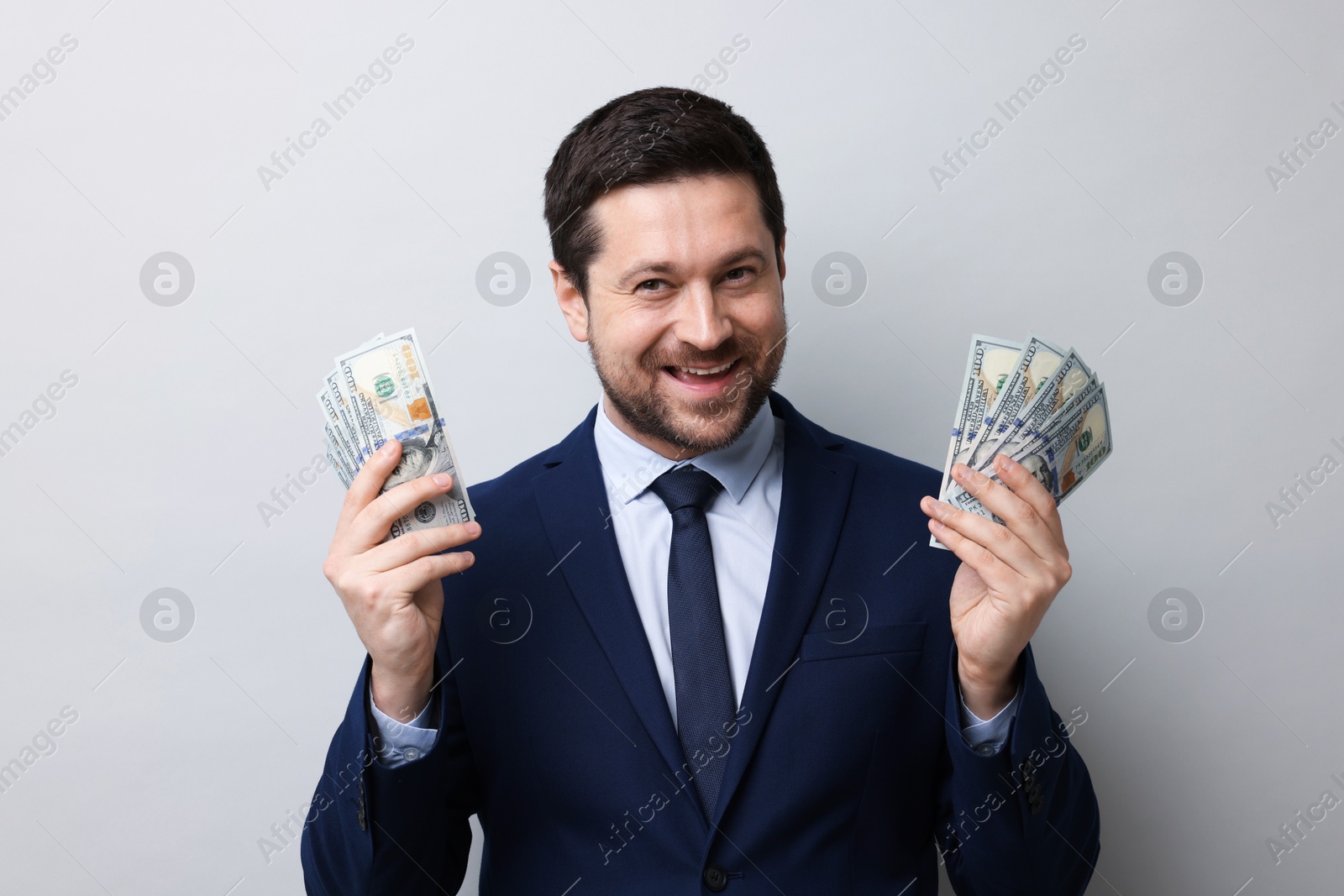 Greedy banker holding dollar banknotes and smiling on grey background Photo of Greedy banker holding dollar banknotes and smiling on grey background
