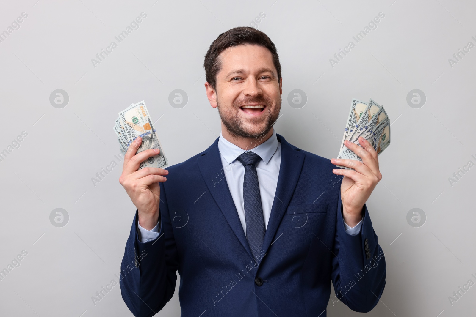 Greedy banker holding dollar banknotes and smiling on grey background Photo of Greedy banker holding dollar banknotes and smiling on grey background