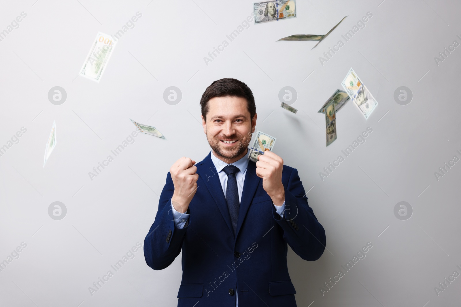 Happy greedy banker under money shower on grey background Photo of Happy greedy banker under money shower on grey background
