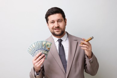 Photo of Greedy banker with dollar banknotes smoking cigar on grey background
