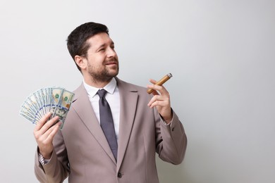 Photo of Greedy banker with dollar banknotes smoking cigar on grey background. Space for text