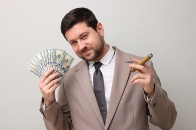Photo of Greedy banker with dollar banknotes smoking cigar on grey background