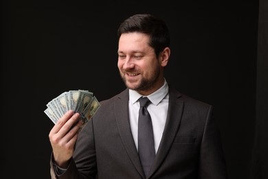 Photo of Happy greedy banker with dollar banknotes on black background
