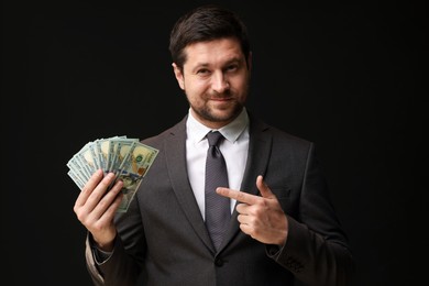 Photo of Greedy banker pointing at dollar banknotes on black background