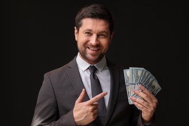 Photo of Happy greedy banker pointing at dollar banknotes on black background