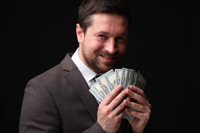 Photo of Happy greedy banker with dollar banknotes on black background