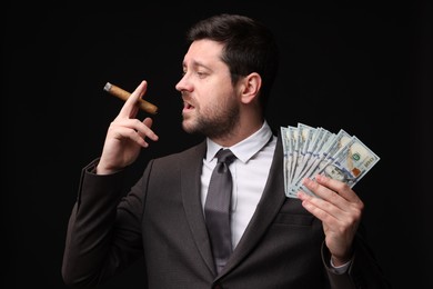 Photo of Greedy banker with dollar banknotes smoking cigar on black background