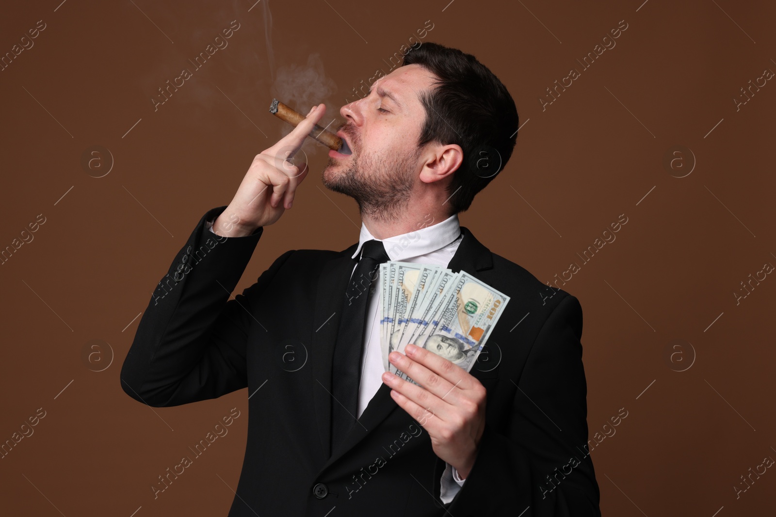 Greedy banker with dollar banknotes smoking cigar on brown background Photo of Greedy banker with dollar banknotes smoking cigar on brown background