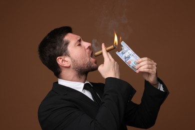 Photo of Greedy banker lighting cigar with dollar banknote on brown background