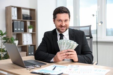 Photo of Happy greedy banker with dollar banknotes at table in office