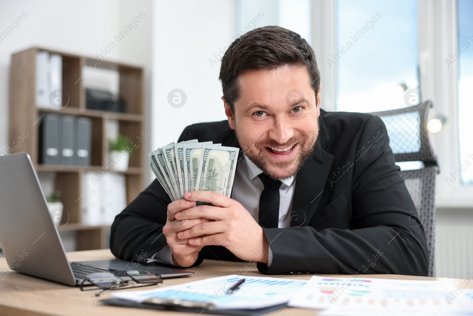 Happy greedy banker with dollar banknotes at table in office Photo of Happy greedy banker with dollar banknotes at table in office