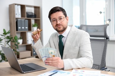 Photo of Greedy banker with dollar banknotes and cigar at table in office