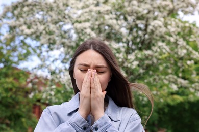 Photo of Woman suffering from seasonal pollen allergy near blossoming tree on spring day