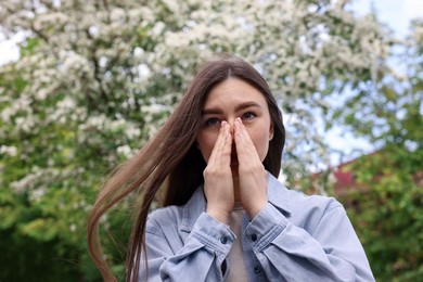 Photo of Woman suffering from seasonal pollen allergy near blossoming tree on spring day