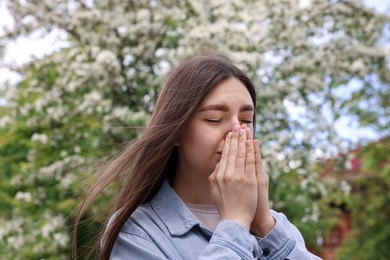 Photo of Woman suffering from seasonal pollen allergy near blossoming tree on spring day