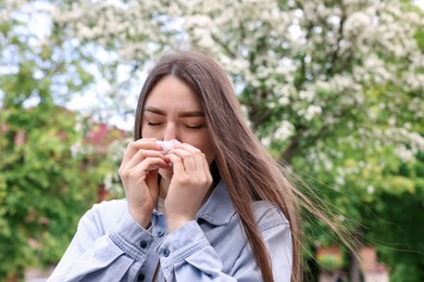 Photo of Woman with paper tissue suffering from seasonal pollen allergy near blossoming tree on spring day