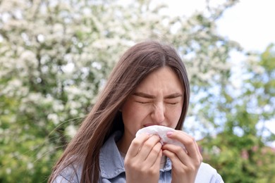 Photo of Woman with paper tissue suffering from seasonal pollen allergy near blossoming tree on spring day