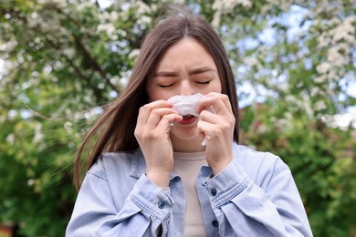 Photo of Woman with paper tissue suffering from seasonal pollen allergy near blossoming tree on spring day
